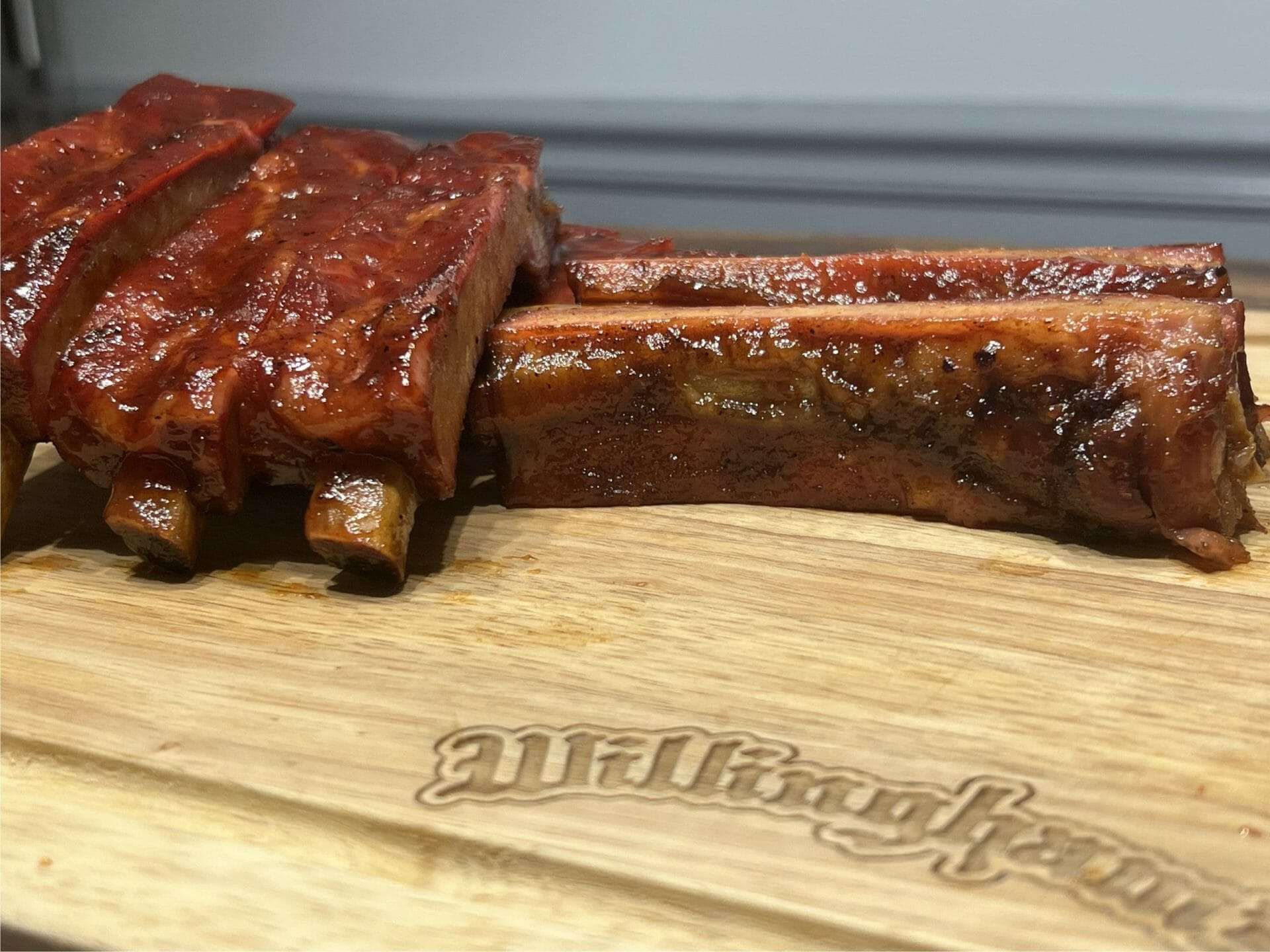 Smoked pork spare ribs on a wooden cutting board, one rib sliced from the rack